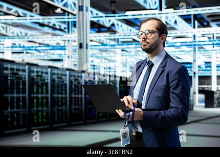 Managing enterprise, laptop and software developer in data center, technology solutions. Supervising operations, notebook application and IT specialist in futuristic server room Stock Photo