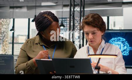 Programmers in office automating workflows using artificial intelligence technology. Teamworking colleagues refining deep learning computational models for faster processing, camera B Stock Photo
