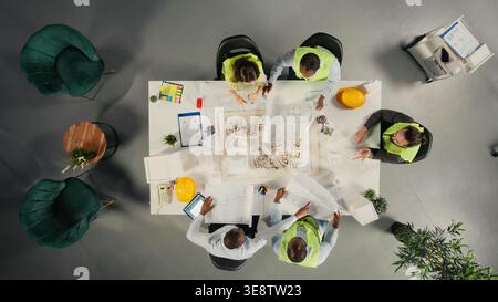 Top down view of developers in modern office environment planning construction. Architects and engineers discuss site preparation, master plan updates and real estate investment. Stock Photo