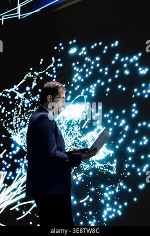 Technician monitors deep learning AI model patterns using laptop. RD lab employee studies artificial intelligence neural network algorithm nodes on digital wall to understand processing using notebook Stock Photo
