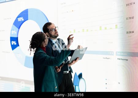 Investors verify company financial statements assets using charts projected on digital wall before securing deal. Financial analysts working together use devices to analyze economic data Stock Photo