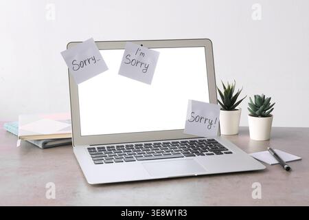 Laptop with word SORRY on sticky notes on grey grunge table Stock Photo