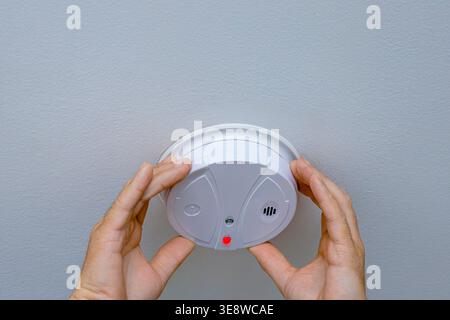 Man installing smoke detector on ceiling at home, checking safety device with indicator light. Fire prevention and residential security concept indoor Stock Photo