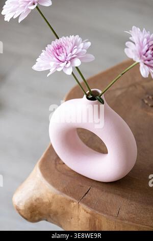 Minimal composition of pink Scandinavian vase with purple daisies, interior decoration on wooden coffee table, white brick wall background Stock Photo