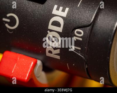 Macro detail of a Rode shotgun microphone showing the brand logo, power symbol, and gain control dial with red shock mount base Stock Photo