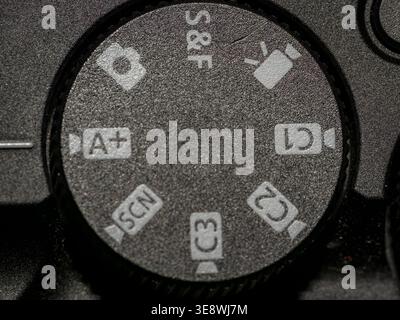 Macro photograph of a camera mode dial with a textured surface, showing various symbols like S&F, C1, C2, and SCN. Stock Photo