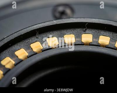 macro closeup of gold plated electronic contacts on a camera lens bayonet mount against blurred black plastic parts Stock Photo