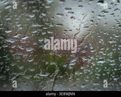 heavy rain drops and water streaks on a glass surface against a soft bokeh background of blurry colors and lights Stock Photo
