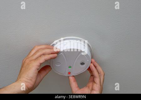 Man installing smoke detector on ceiling at home, checking safety device with indicator light. Fire prevention and residential security concept indoor Stock Photo