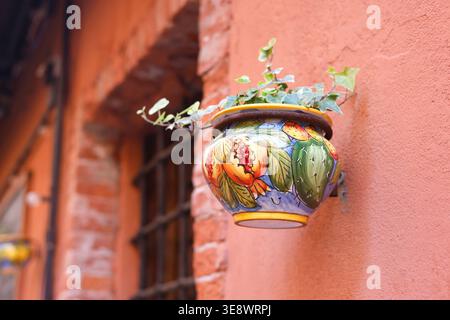 Traditional hand painted Italian ceramic flower pot with ivy on terracotta wall. Close-up shot features colorful Mediterranean pottery with Stock Photo