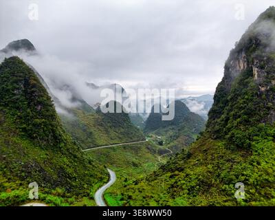 Aerial view of the winding mountain road of the Ha Giang Loop passing through lush green karst peaks and misty valleys in Vietnam. Stock Photo
