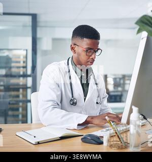 Black man, typing or doctor with computer in hospital for medical report, research or insurance info. Desktop, person and healthcare professional with Stock Photo