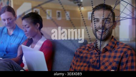 Smiling bearded man in plaid shirt sitting right on couch in lounge, with laptop and divider Stock Photo