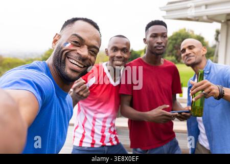 African American men on deck, man in blue T-shirt taking smartphone selfie celebrating goal Stock Photo