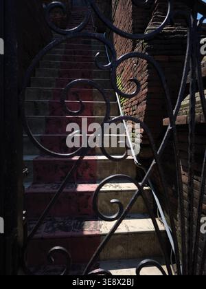 A staircase leading up with an old brick wall and a classic fence in the foreground with dramatic lighting Stock Photo