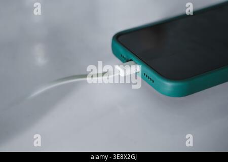 A detailed, shallow depth-of-field shot of a mobile phone in a teal green protective case connected to a white charging cable. Stock Photo