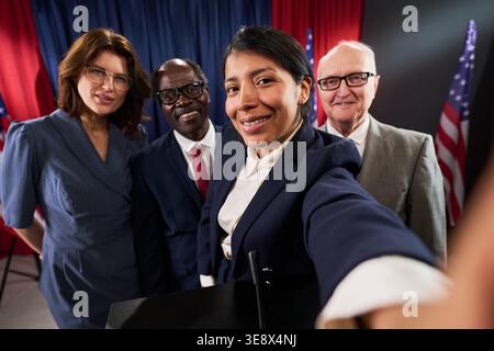 POV of diverse political candidates taking selfie near podium with American flags, presenting election campaign teamwork and leadership. Useful for voting, democracy, public affairs marketing Stock Photo