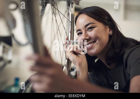 Happy, woman and repair in bicycle shop with maintenance, wheel restoration or quality assurance. Female person, smile and mechanic in small business Stock Photo