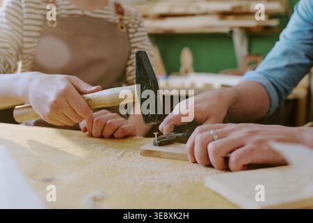 Adult Woman Teaching Child Hammering Nail in Woodworking Class Stock Photo