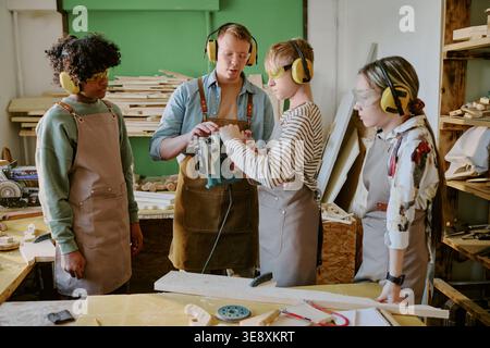 Adult Man Guiding Teenagers Using Jigsaw in Carpentry Class Stock Photo