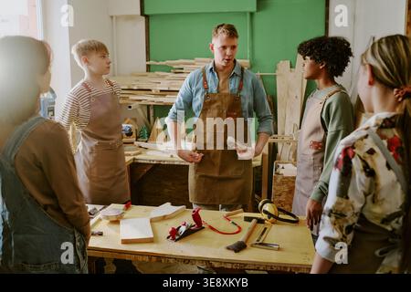 Adult Man Instructing Diverse Teenagers in Woodworking Class Stock Photo