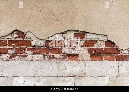 Peeling plaster reveals weathered red brick and cracked stucco on an aged urban building facade, conveying decay, texture, and rustic architectural de Stock Photo