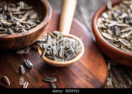 Sunflower seeds piled in a wooden spoon and bowls on a rustic cutting board, showing textured shells and natural tones. A healthy, crunchy snack and i Stock Photo