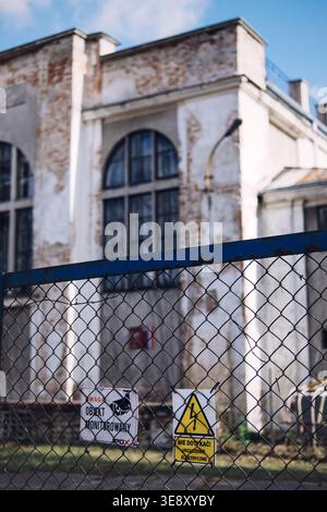 warning signs stands before old industrial building. Vacant property security, industrial asset protection, facility management risks. Stock Photo