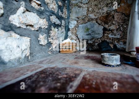 Color photograph of worn books stacked in a rough stone corner on tiled flooring, with textured masonry walls and shallow depth of field in a rustic i Stock Photo