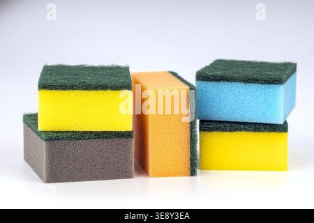 Collection of colorful kitchen sponges stacked together featuring bright yellow, orange, and blue foam layers paired with durable green scrubbing pads Stock Photo