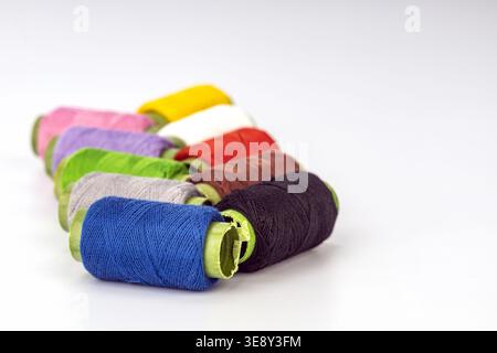 A collection of vibrant thread spools with lime green tape arranged in a diagonal line against a clean white background. Colors include royal blue, bl Stock Photo