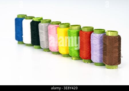 Professional assortment of ten vibrant thread spools with distinctive lime green caps arranged in a diagonal line. Features a rainbow of colors includ Stock Photo