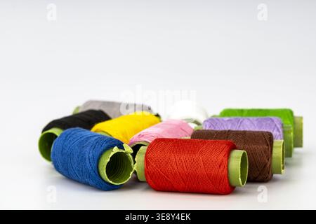 Organized array of vibrant thread spools in various colors including blue, red, yellow, pink, purple, brown, black and white, each with bright green b Stock Photo