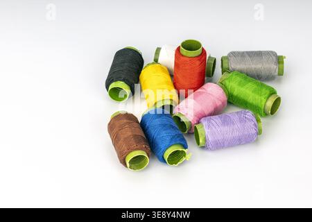 Nine assorted colorful thread spools featuring vibrant hues of dark gray, yellow, bright red, pink, purple, lime green, royal blue, brown, and cream. Stock Photo