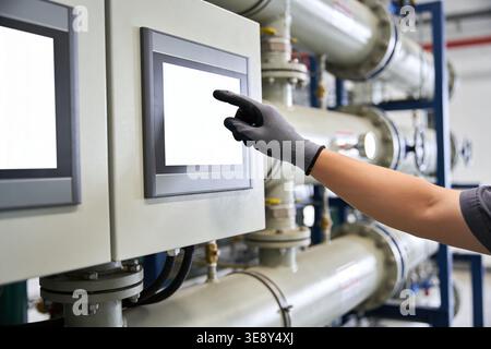 Close-up of a gloved hand interacting with a digital interface in a factory setting with complex machinery in the background Stock Photo