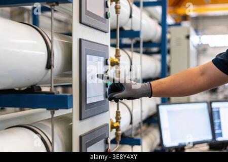 A close-up view of a person wearing a protective glove interacting with a digital interface on a complex industrial machine Stock Photo