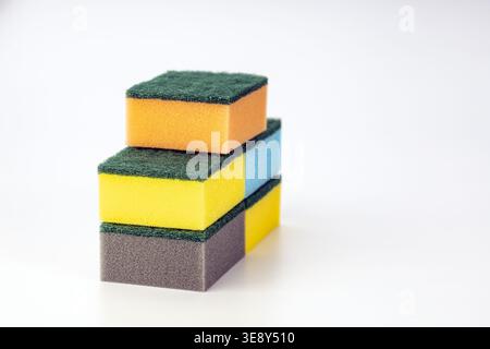 Stack of three colorful kitchen cleaning sponges with bright yellow, warm orange, and gray foam cores, each topped with dark green abrasive scrubbing Stock Photo