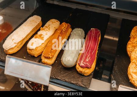 Assorted eclairs displayed in bakery shop showcase, colorful glazed desserts on tray. Concept: indulgent food temptation Stock Photo