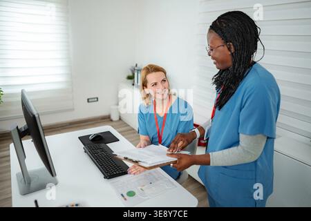 Two diverse female nurses collaborating and discussing documents in a medical office Stock Photo