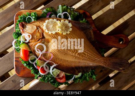 Smoked flounder fish (savukampela) served on rustic wooden board with kale, tomatoes, and lemon, traditional nordic seafood, artisan food Stock Photo