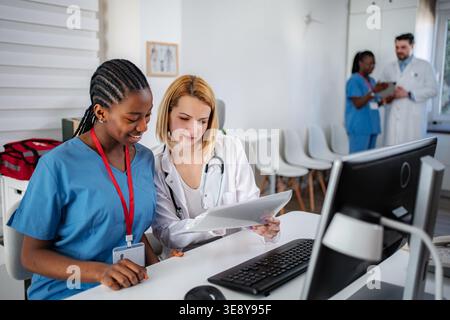 Two female doctors reviewing patient files on a digital tablet at the hospital Stock Photo