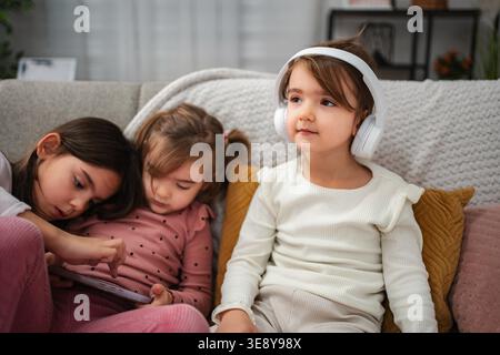 Two preschool age girls sitting on a couch, using a digital tablet and listening with headphones Stock Photo