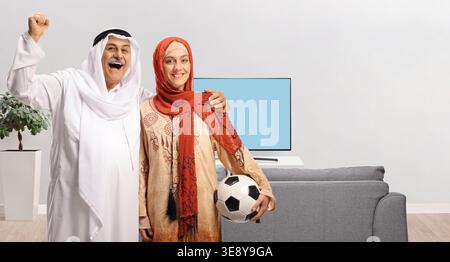 Middle eastern couple football fans cheering in front of tv at home Stock Photo