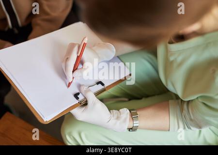 Close up of middle aged female caregiver writing notes on clipboard during senior care visit in nursing home Stock Photo