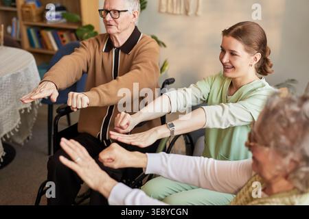 Senior residents exercising with young female caregiver in nursing home, supporting mobility and active aging Stock Photo