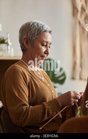Vertical shot of senior Asian woman knitting in nursing home, supporting active aging, fine motor activity, daily care routine Stock Photo