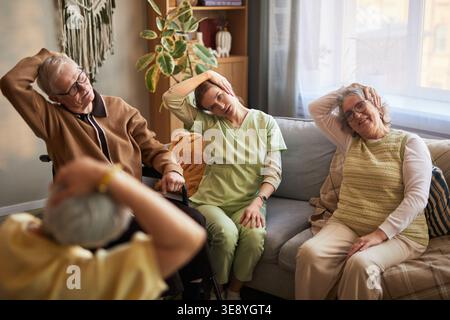 Senior men and women with female caregiver stretching necks during group exercise in nursing home, supporting mobility and elder care Stock Photo