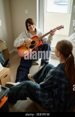 Man Playing Guitar for Girlfriend during Home Move Stock Photo