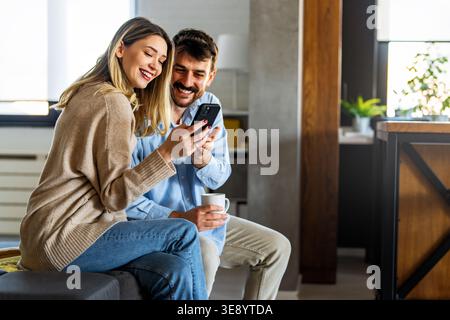 Young happy multiethnic couple having fun while using laptop, digital device at home Stock Photo