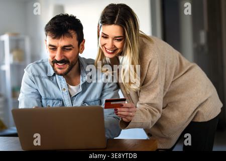 Smiling happy couple working on an e-commerce business at home using laptop and credit card Stock Photo
